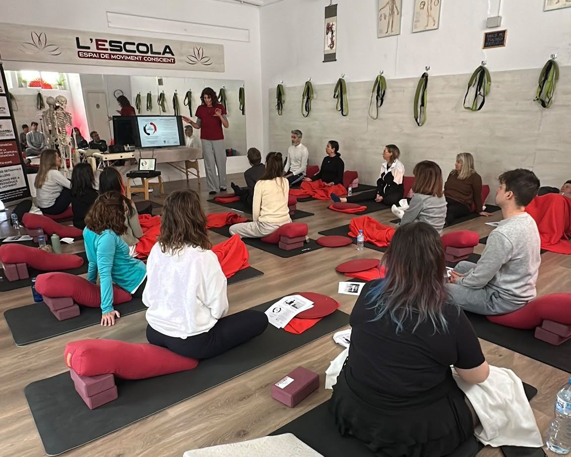Grup en un taller de L'Escola, asseguts sobre estores seguint l'explicació